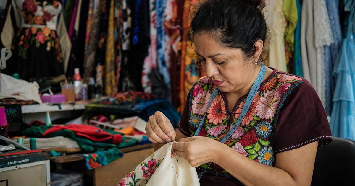 Una persona trabajando en una boutique de ropa en México, cosiendo un detalle en una prenda con telas y una cinta métrica alrededor.